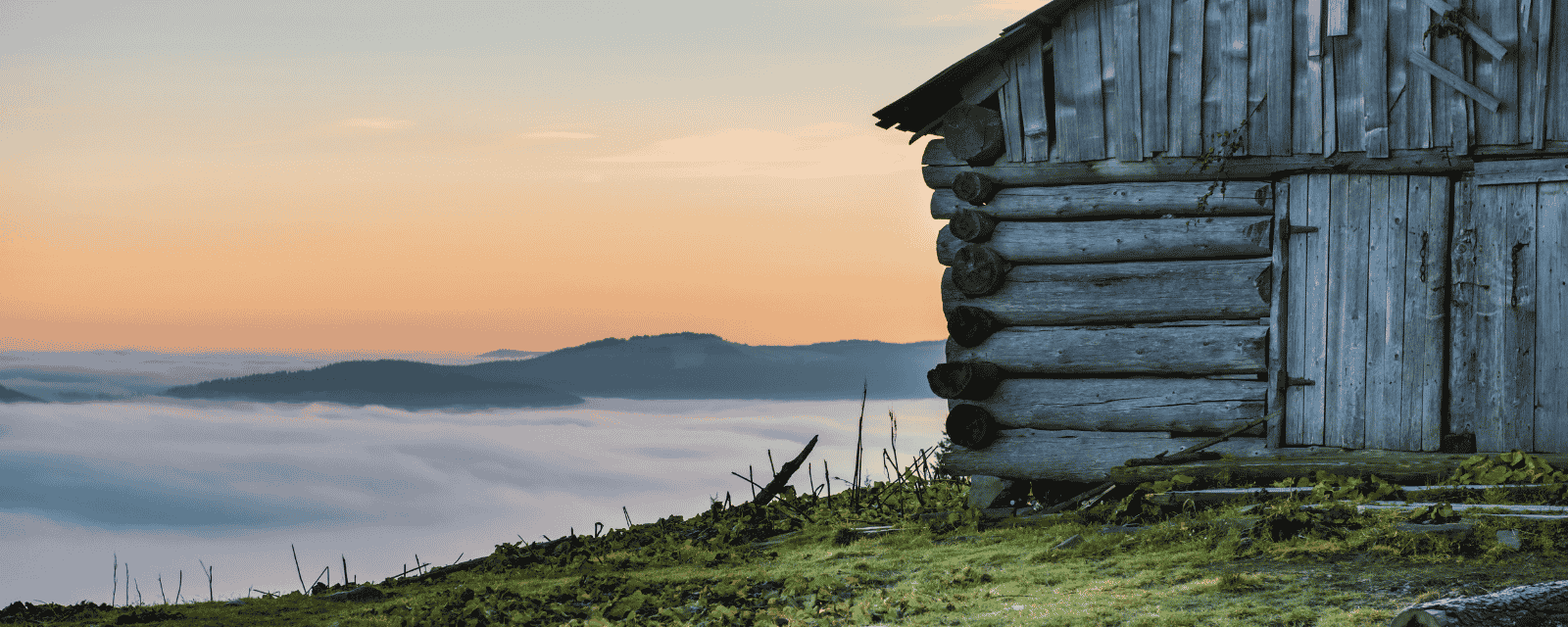 A wooden mountain cabin at sunrise, above a sea of clouds
