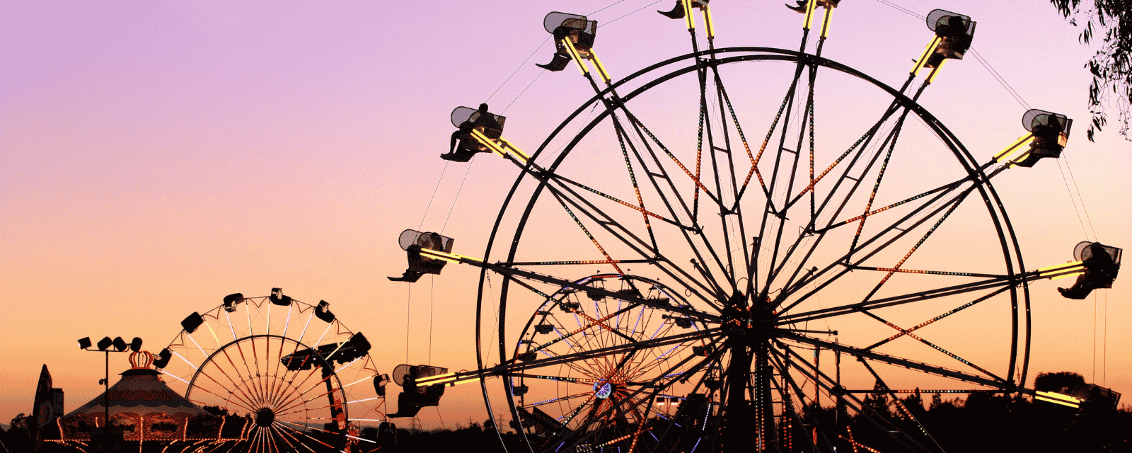 A ferris wheel and fairground rides silhouetted against a pink and orange sunset sky