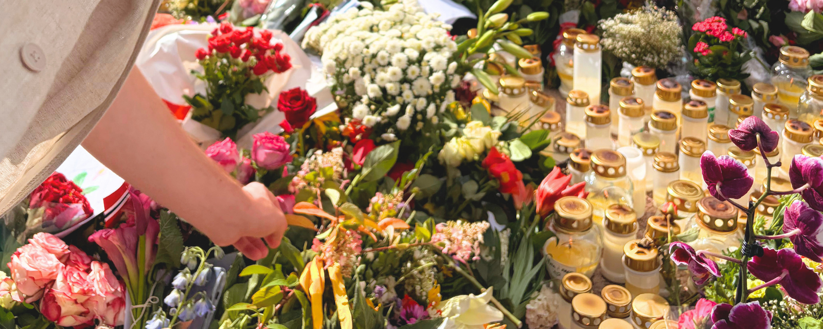 A hand arranging flowers among memorial candles and bouquets left in tribute