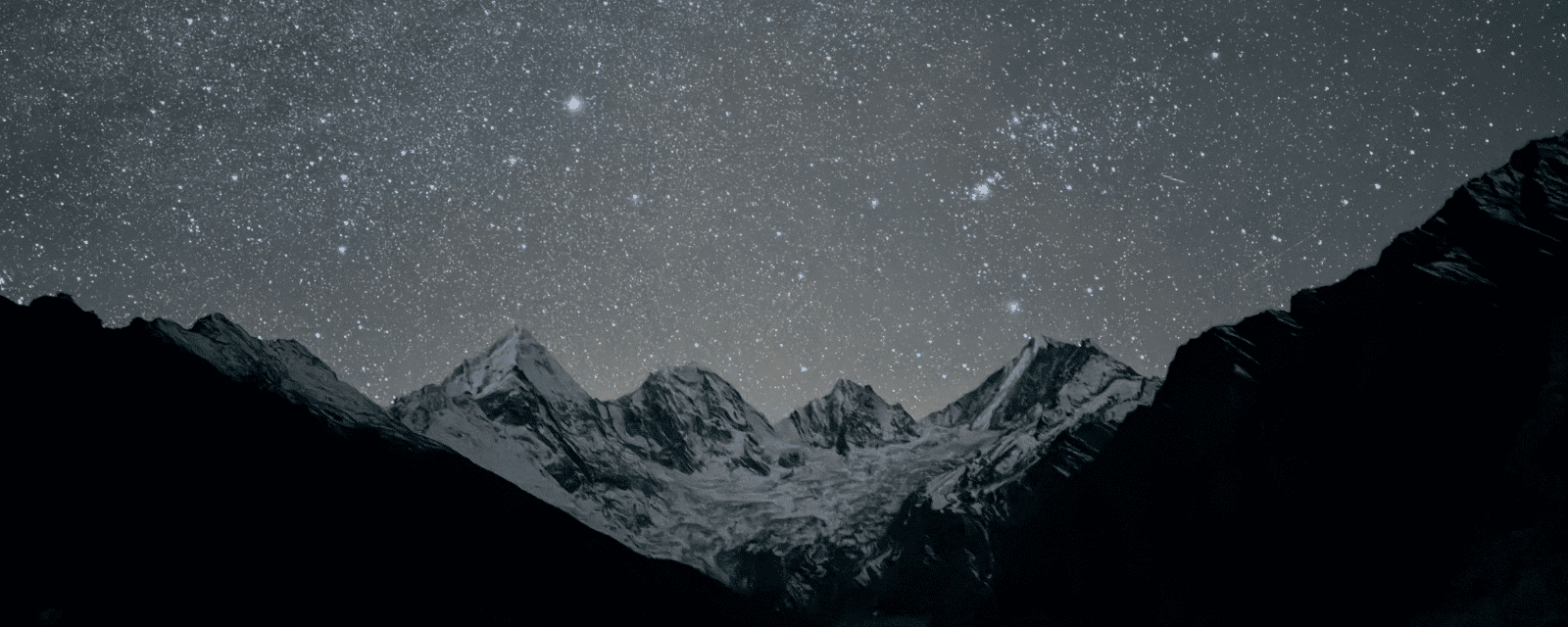 A starry night sky over dark, snow-capped mountain peaks